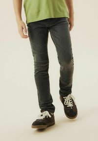 Jean gris foncé à coupe slim, avec un léger délavage. Associés à des baskets marron, mettant en avant des lacets blancs et une surface texturée.