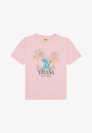 T-shirt di cotone rosa con una grafica di un personaggio blu con palme. Il testo recita "'OHANA significa famiglia" in nero. Maniche corte, colletto a girocollo.
