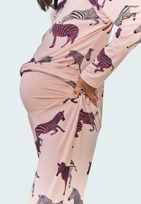 Ein hellrosa Kleid aus Stoff mit einem wiederholten Zebra-Druck in Schwarz und Dunkelpink. Das Kleid hat eine figurbetonte Form mit gerafften Seiten.