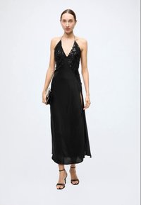 Black halter neck dress with sequin detailing at the bodice, flowing fabric, side slit, and paired with strappy heels and a clutch.