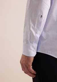 Camicia azzurro chiaro con motivo a cerchi, dotata di polsini con bottoni e un delicato dettaglio ricamato sulla manica. Tessuto liscio.