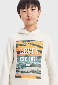 Sudadera blanca con un estampado gráfico que presenta franjas naranjas, verdes y azules. El diseño incluye "LEVI'S EST. 1873" destacado.