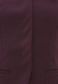 Burgundy bleiseri, jossa on sileä kangas, istuva leikkaus, terävät läpät ja kaksi etutaskua. Yksinkertainen ja strukturoitu muotoilu.