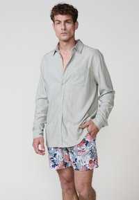 Lichtgrijze lange mouw shirt met een button-down kraag en borstzak, gecombineerd met zwemshorts met kleurrijk bloemenpatroon.