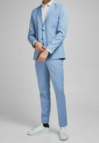 Ljusblå skräddarsydd kostym med slim fit, med två knappar och slagkrage, i kombination med en mönstrad skjorta och vita sneakers.