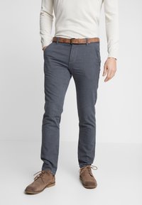 Šedé bavlněné kalhoty slim fit s texturovanou látkou, bočními kapsami a hnědým koženým opaskem. Kombinované s hnědými semišovými botami.