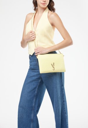 Borsa a tracolla gialla trapuntata con catena dorata e dettagli del logo, abbinata a una blusa giallo chiaro e jeans a vita alta.