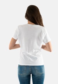 Camiseta de algodón blanca con mangas cortas, cuello redondo, textura suave, combinada con jeans azules que presentan un patrón de costura de bolsillo distintivo.