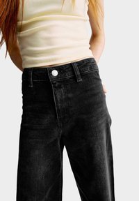 Hoge taille zwarte denim broek met een iets losse pasvorm, voorzien van een metalen knoop aan de voorkant, klassiek vijf-pocket ontwerp en subtiele textuur.