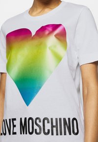 Bílý bavlněný tričko s velkou, vícebarevnou gradientovou grafikou srdce v růžové, zelené a modré barvě. Černý text "LOVE MOSCHINO" na spodní části.