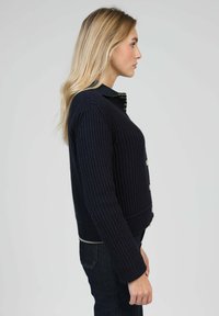 Pull côtelé bleu marine avec un col structuré, des boutons dorés et des manches longues. Le tissu présente un motif texturé pour plus de détails.