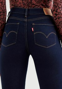 Högmidjade mörk denimjeans med guldtråd, med en distinkt fickdesign i form av ett hjärta och en läderlogopatch bak.