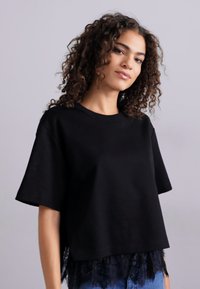 Czarna krótka koszulka z szerokimi rękawami, wykonana z gładkiej bawełny, z koronkowym wykończeniem na dole, które dodaje faktury i detalu.