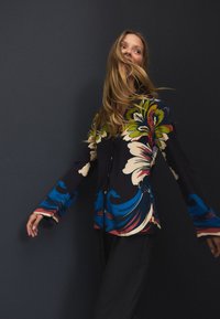 Chemise à boutons à motifs floraux avec manches longues, présentant des couleurs vives comme le bleu, le vert et le rouge sur un fond sombre.