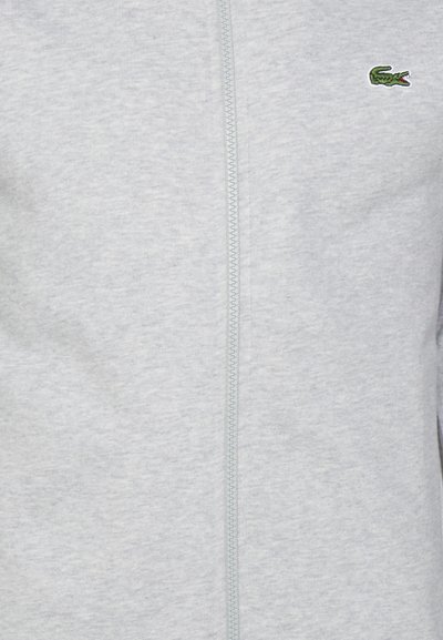 Сив суитшърт с цип, изработен от мек плат, с зелен логотип на крокодил Lacoste в горния ляв ъгъл и преден цип.