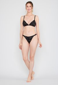 Černý bikinový set s trojúhelníkovým braletem s tenkými ramínky a odpovídajícími nízkými kalhotkami, obě zdobené jemným zlatým vzorem.