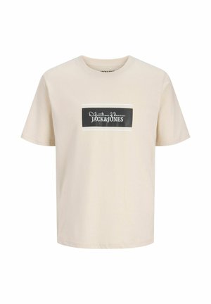 Jasnobeżowa koszulka z krótkim rękawem z czarną, prostokątną naszywką z logo na piersi z napisem "Jack & Jones" białym tekstem.