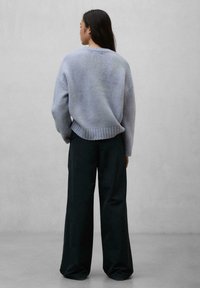 Light blue knitted sweater with wide sleeves and ribbed hem, paired with loose black trousers, presented from a back view against a plain background.