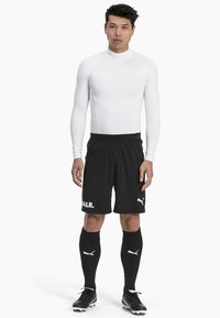 Hvit langermet treningsskjorte, sorte shorts med logo, sorte leggsokker og sorte fotballsko, alt designet for sportsytelse.