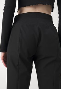 Pantalons noirs ajustés avec une texture lisse, dotés d'une taille mi-haute, de poches cachées et d'une coupe moderne et épurée.