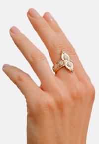 Gold ring featuring oval moonstones set in a decorative band with ornate accents. Smooth texture and intricate detailing enhance its design.