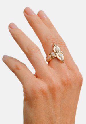 Bague en or ornée de pierres de lune ovales, montées sur une bande décorative aux accents raffinés. Sa texture lisse et les détails complexes rehaussent son design.