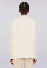Maglione a maniche lunghe in beige cremoso, con colletto alto, vestibilità rilassata e texture morbida. Design semplice e minimale con spacchi laterali.