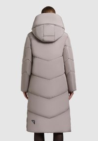 Polstret lang frakke i lys beige, med en stor hætte og v-formet quiltet design. Afsluttet med et lille brandlogo nederst til venstre.