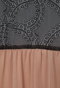 Superposition de dentelle florale noire sur un tissu rose pâle transparent froncé, détail textile en gros plan.