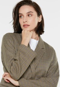 Brown and blue check-patterned blazer with a tailored design, soft texture, and lapel collar. Features a relaxed fit and visible seams.