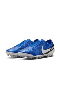 Botas de fútbol sintéticas azules con parte superior texturizada, swoosh de Nike blanco, acentos negros y tacos cónicos sobre una suela blanca.