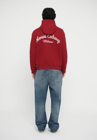 Rød hættetrøje med "Armani Exchange Milano" logo på ryggen, parret med løpske blå denim jeans; afslappet pasform, minimal design.