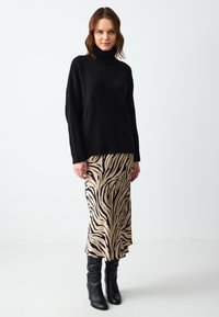 Maglione nero a collo alto lavorato a maglia abbinato a una gonna beige con strisce zebrate nere, completato da stivali neri al ginocchio.