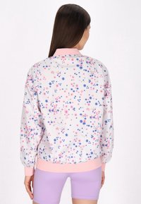 Bloemige bomberjack met een witte basis, voorzien van roze en blauwe bloempatronen, elastische manchetten en een roze kraag. Aansluitende pasvorm.