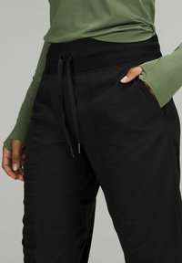 Schwarze Jogginghose mit gerippter Textur und elastischem Bund, kombiniert mit einem grünen Langarmoberteil mit Daumenlöchern.