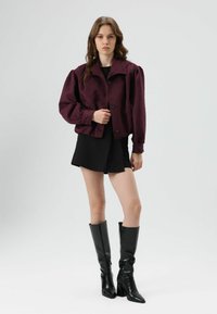 Bordeaux cropped jack met pofmouwen, knopen aan de voorkant, gecombineerd met een zwarte minirok en zwarte kniehoge laarzen. Glad stofoppervlak.