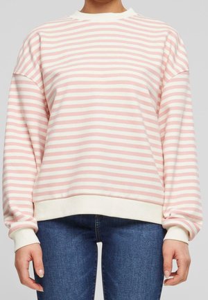 Persona vestida con un suéter de rayas horizontales blancas y rosas de manga larga con puños acanalados y jeans azules, vista desde el cuello hasta las caderas.