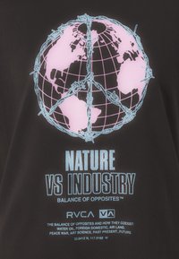 Sort bomulds T-shirt med et grafisk motiv af en globus med pink kontinenter og blå pigtråd. Teksten lyder: "NATURE VS INDUSTRY" i blå.