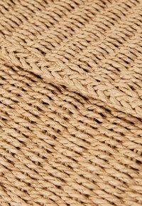 Natural woven storage basket made of beige textured fibers, featuring a tight, intricate braid pattern with a soft, flexible shape.