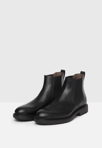 Bottines Chelsea en cuir noir avec des panneaux latéraux élastiques, bout arrondi et semelle en caoutchouc texturé. Design épuré, accents minimalistes et construction robuste.
