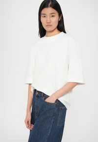 Hvit T-skjorte med kort erme og løs passform, laget av myk bomull. Kombinert med høytaljede blå denimjeans med klassisk knappeåpning.