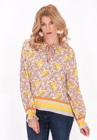 Blusa a maniche lunghe con motivo floreale giallo e arancione, caratterizzata da un colletto a fessura e polsini arricciati, con orlo a righe.