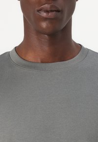 Grau Baumwoll-T-Shirt mit Rundhalsausschnitt, glatter Textur und kurzen Ärmeln, mit einem gerippten Kragen und minimalistischen Nähten.