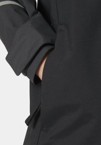 Czarna kurtka o eleganckim, nowoczesnym designie z zasuwaną kieszenią i kontrastującym szarym paskiem na rękawie. Gładka tekstura materiału.