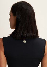Top nero senza maniche con una texture liscia, caratterizzato da un piccolo etichetta logo sulla parte posteriore vicino al colletto. Design semplice ed elegante.