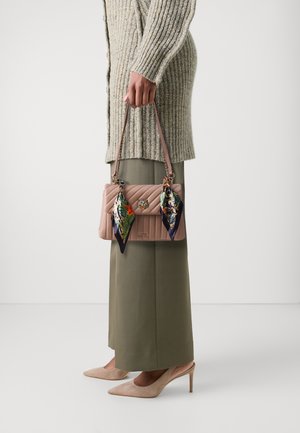 Sac à main matelassé rose avec des écharpes décoratives, quincaillerie en argent et une bandoulière en chaîne. Porté avec un pull en tricot surdimensionné et un pantalon ajusté.