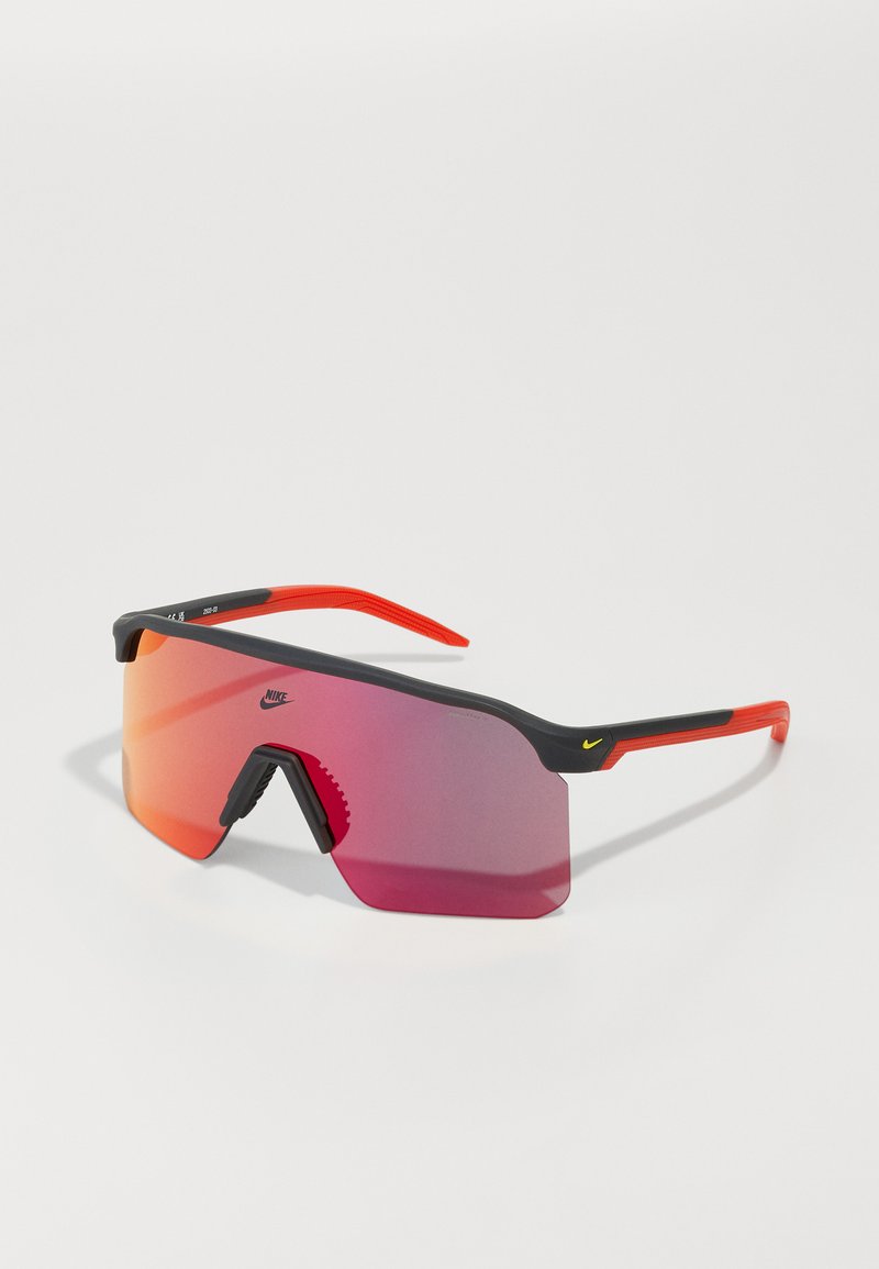 Gafas de sol deportivas Nike con un diseño envolvente, lentes tintados en rojo, montura negra, acentos naranjas y almohadilla nasal texturizada para un mejor agarre.