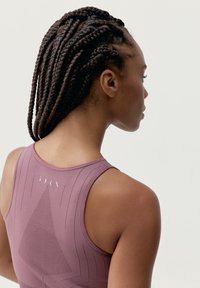 Ribota sportinė marškinėlių viršūnė dulkėtai mauve spalvos, su geometriniu dizainu ir logotipo detale nugaroje. Lygus paviršius ir prigludusi forma.