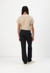 Camiseta de manga corta beige combinada con pantalones negros, con un corte relajado. Los pantalones tienen un bolsillo trasero y se llevan con zapatillas de color claro.