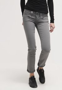 Grå slim-fit jeans med en strukturerad yta, fem-ficksdesign, knappstängning och uppvikta benslut, kombinerat med svarta sneakers.